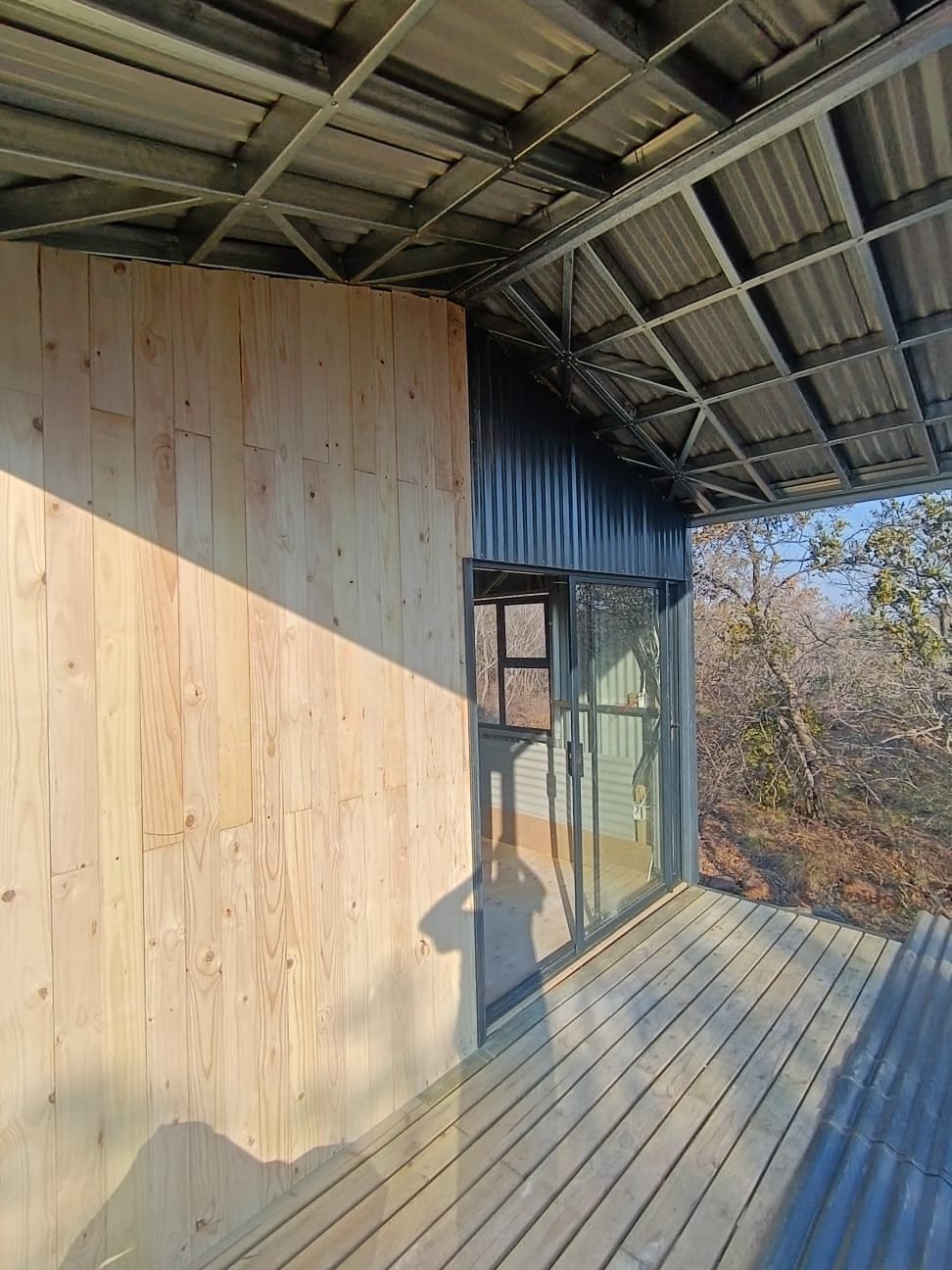 Finished tiny home deck with timber cladding and sliding glass door overlooking bushveld, South Africa