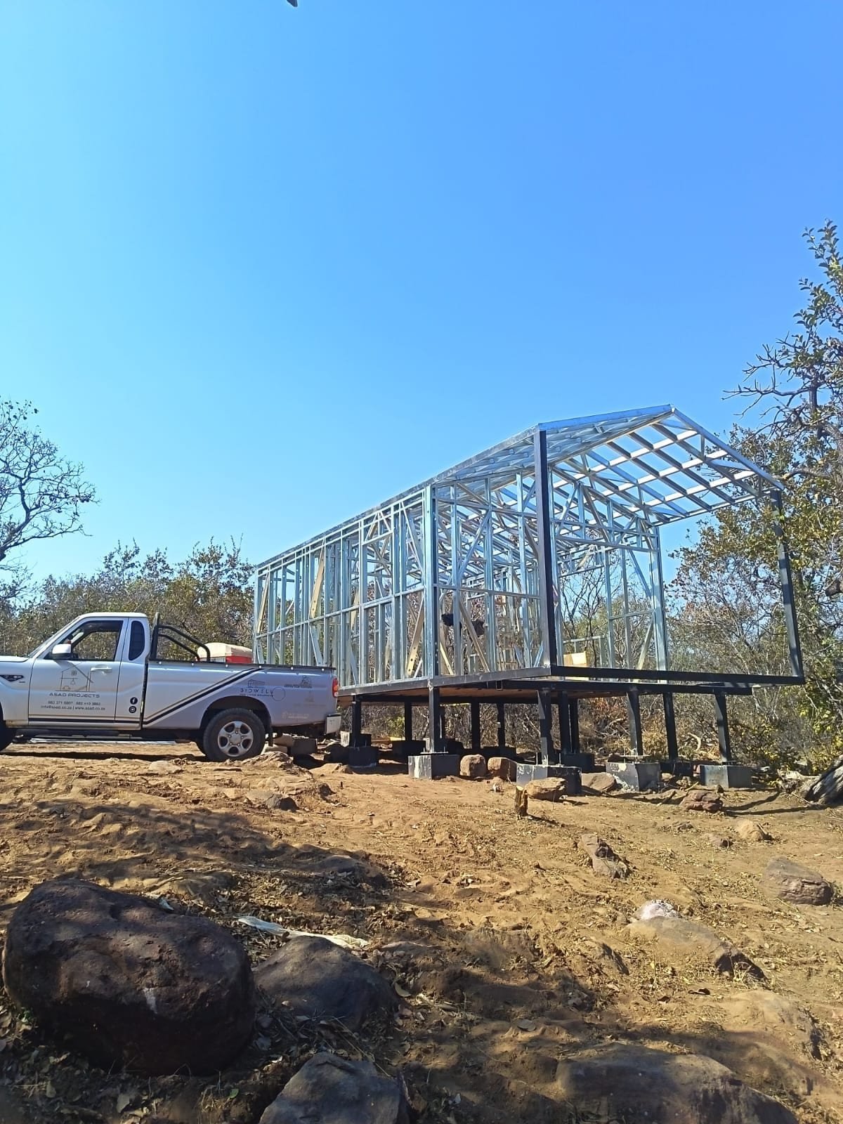 Elevated steel frame tiny home under construction with Asad Projects vehicle, South Africa